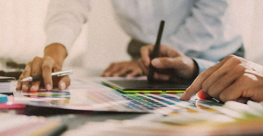 Two colleagues sorting through pages of color swatches on a desk