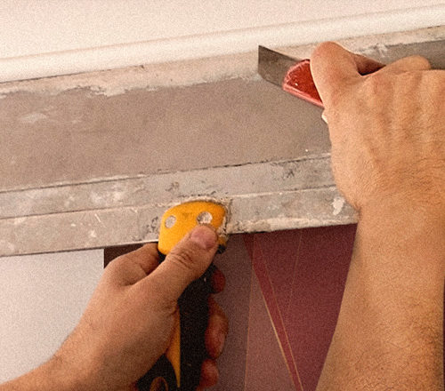 Hands holding up work tools to install wall covering at the top of a wall