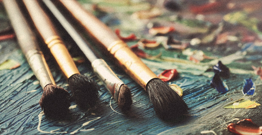 paint brushes lying on a palette covered in oil paint of various shades